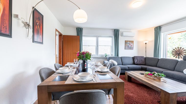 Een moderne woonkamer met een elegante bank en een eettafel. Veel ramen zorgen voor veel licht en een gezellige sfeer.