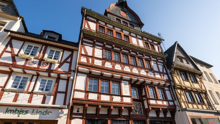 Ein historisches Fachwerkhaus mit bunten Verzierungen und einem reetgedeckten Dach. Die Sonne scheint klar am blauen Himmel.