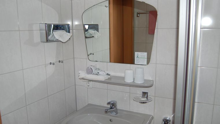 Een moderne badkamer met een wastafel en een spiegel. De muren zijn licht betegeld, en enkele handdoeken zijn netjes neergelegd.