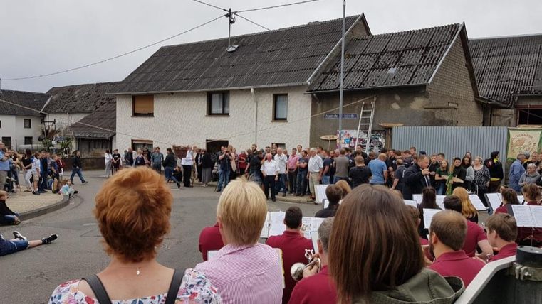 A crowd has gathered at a street festival in front of a building. Many people are standing together, watching the event.