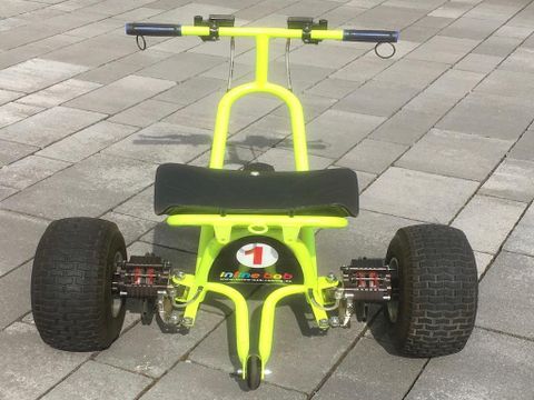 Ein leuchtend gelbes und schwarzes Kettcar mit großen Reifen steht auf einem gepflasterten Boden. Das Fahrzeug scheint für Kinder zum Spielen gedacht zu sein.