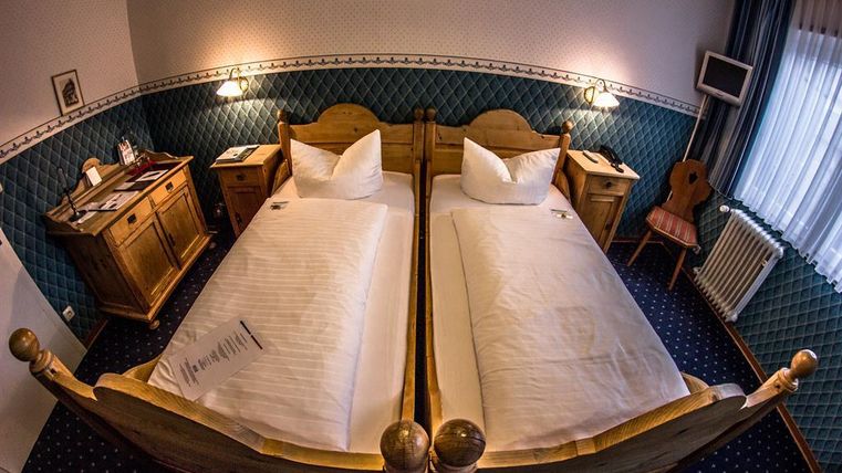 A cozy bedroom with two single beds and wooden interiors. Next to the beds are a desk and a chair, and the room has a warm atmosphere.