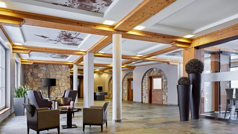 A modern hotel lobby with wooden details and elegant furniture. The light falls softly on the stone floor and walls.
