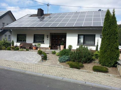 A modern house with solar panels on the roof. The garden is well-maintained and has various plants and shrubs.