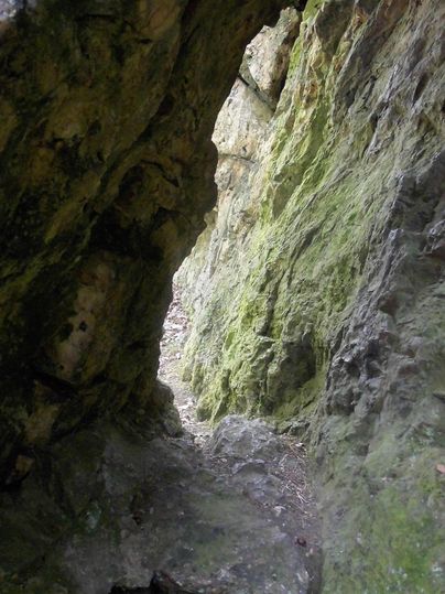 A narrow path leads through a rock opening. The walls are surrounded by moss-covered stone.