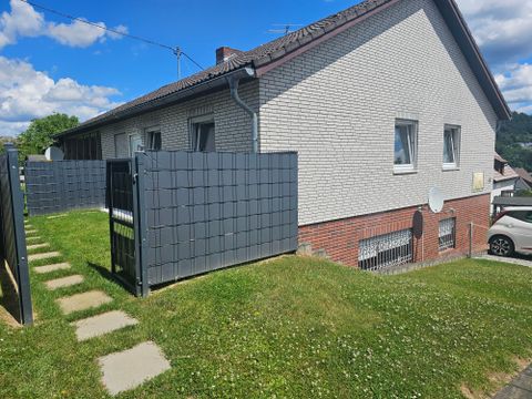 A simple residential house with a garden and green lawn. A privacy fence surrounds the outdoor area and the sky is partly cloudy.