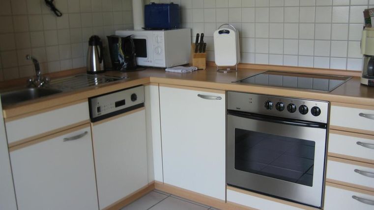 Une cuisine moderne avec des armoires claires et une plaque de cuisson en acier inoxydable. On peut également voir un évier, un four à micro-ondes et divers ustensiles de cuisine.