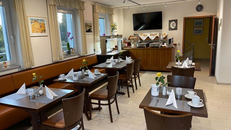 Een vriendelijk café met tafels en stoelen. De tafels zijn mooi gedekt en er is een selectie van dranken en snacks.