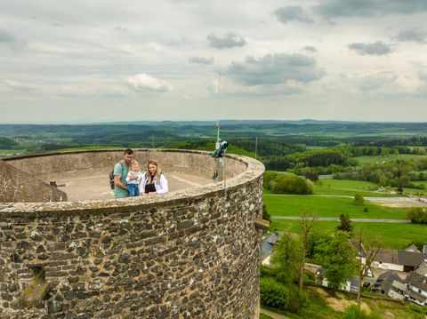 Een gezin staat op een oude toren en geniet van het uitzicht. Op de achtergrond strekt zich een groene landschap uit onder een bewolkte lucht.