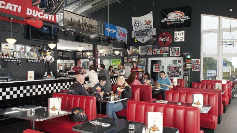 Un diner élégant avec des sièges rouges et des accessoires de moto sur les murs. Les clients savourent leur repas dans une ambiance conviviale.