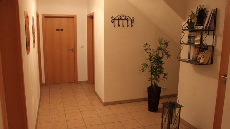 A bright hallway with a plant and a shelf on the wall. Pictures hang on the wall and there is a door to a room.
