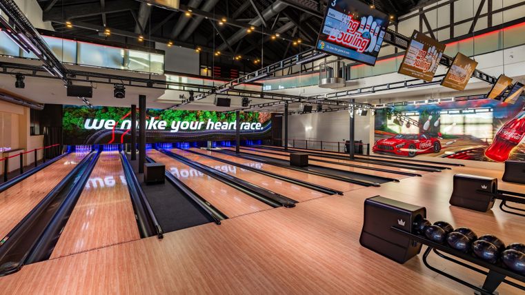 A modern bowling alley with multiple lanes and large screens. The decor is bright and inviting.