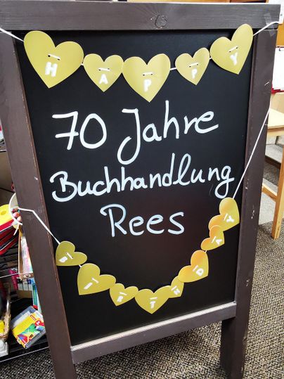 A black sign celebrates the 70th anniversary of the Rees bookstore. It is decorated with golden hearts and the inscription "Happy."