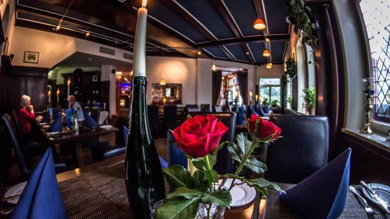 An elegant restaurant with a blue ceiling and set tables. On the table are a candle and fresh red roses.