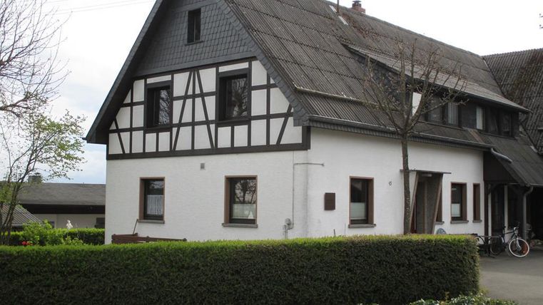Ein traditionelles Haus mit Fachwerk-Elementen und einem begrünten Vorgarten. Die Fassade ist hell und die Dachkonstruktion ist modern.