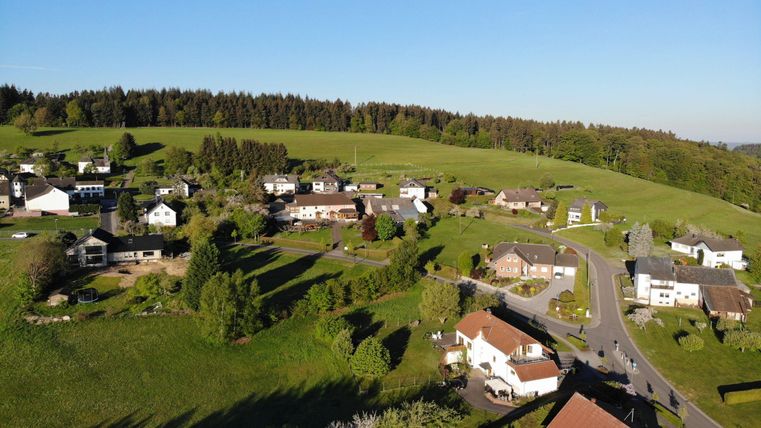 Een schilderachtig landschap met verschillende huizen en groene weiden. Op de achtergrond zijn beboste heuvels te zien.
