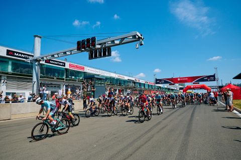 Eine Radrennbahn mit vielen Fahrern, die im Wettkampf sind. Im Hintergrund sind Zuschauer und Rennbanner zu sehen.