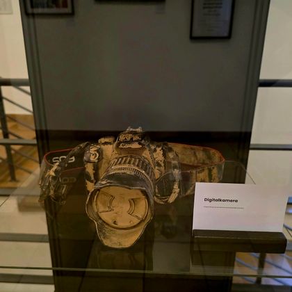 An old camera in a display case. Next to it is a sign with the designation of the object.