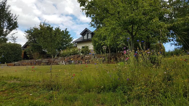 Ein schönes Haus umgeben von Bäumen und grünen Wiesen. Der Himmel ist teilweise bewölkt.