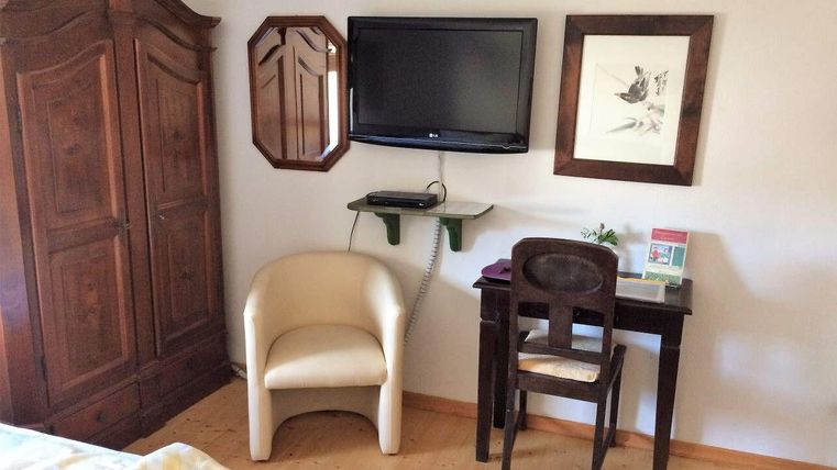 Een gezellige kamer met een houten kledingkast, een televisie en een klein bureau. Een comfortabele stoel nodigt uit om te ontspannen.