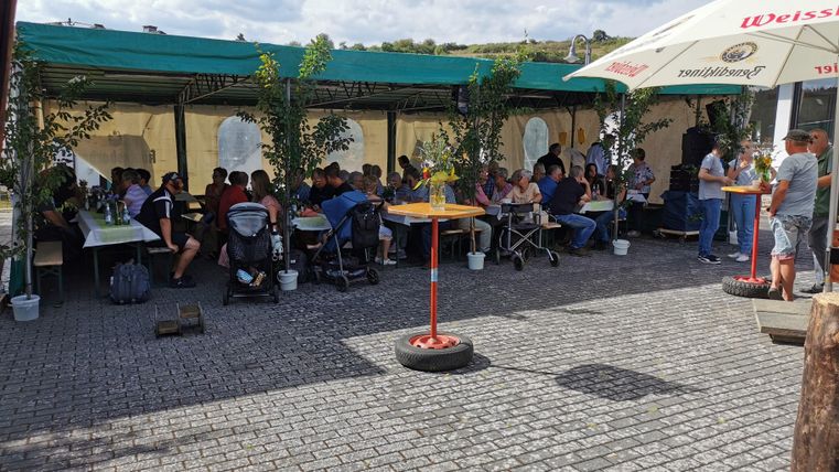 Ein überdachter Außenbereich mit vielen Gästen, die an Tischen sitzen. Die Atmosphäre wirkt gesellig und einladend.