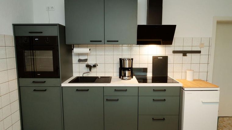 Eine moderne Küche mit grünem Möbel und weißen Wänden. Sie enthält einen Herd, einen Kühlschrank und eine Kaffeemaschine.