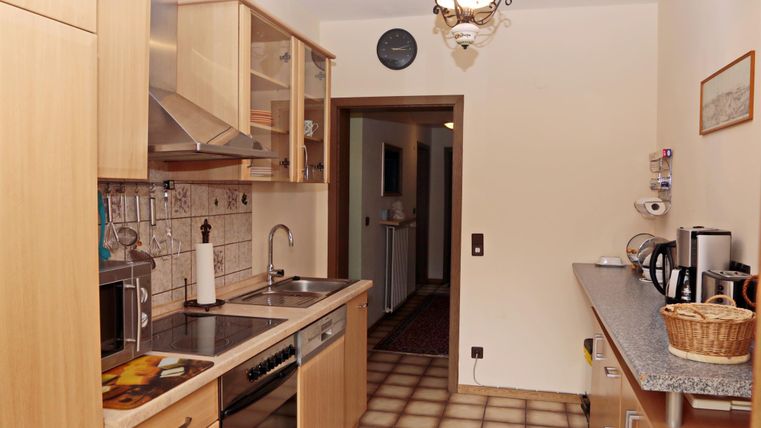 Een moderne keuken met houten kasten en een goed uitgeruste werkplek. Op de achtergrond is een gang te zien.