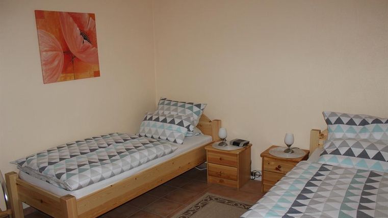 A simple room with two single beds and colorful bed linens. A colorful picture hangs on the wall and there are small nightstands next to the beds.