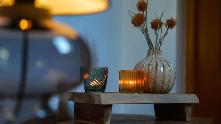 Een stijlvolle tafelversiering met kaarsen en een vaas. Op de achtergrond straalt een lamp zachtjes.