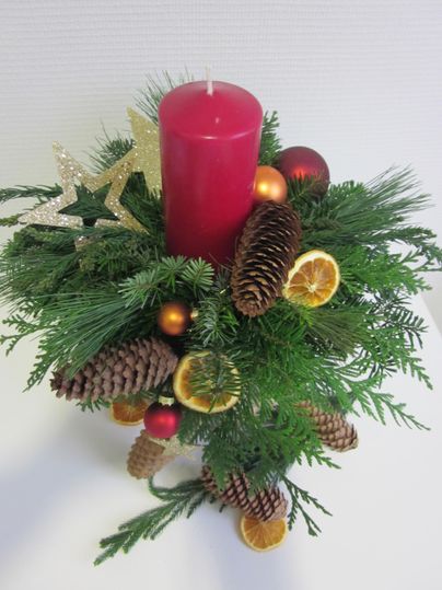 Ein festlicher Adventskranz mit einer roten Kerze, Tannenzweigen und dekorativen Elementen. Kiefernzapfen und getrocknete Orangenscheiben verleihen einen warmen Touch.