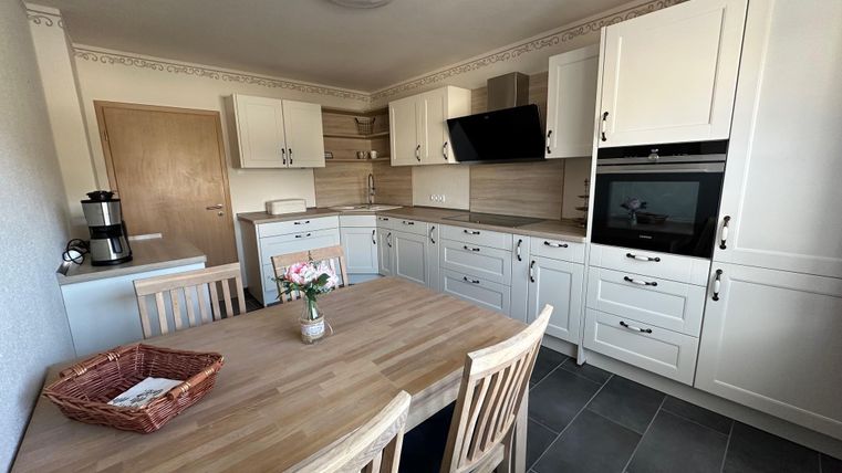 Een moderne keuken met witte meubels en een grote houten tafel. De ruimte is licht en goed uitgerust.