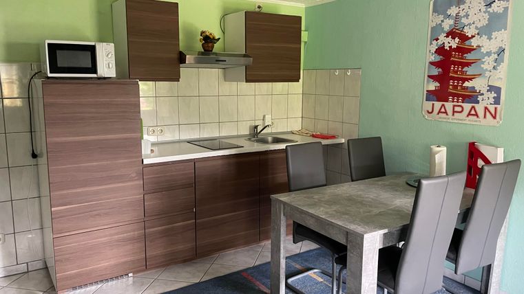 A modern kitchen with a dining table and chairs. The walls are painted in a soft green hue, and there is a Japanese wall decoration.