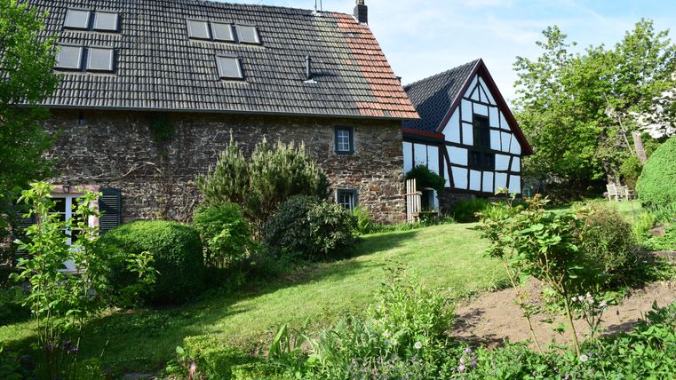 A charming property with a stone house and a half-timbered house. The garden is green and well-maintained, surrounded by beautiful plants.