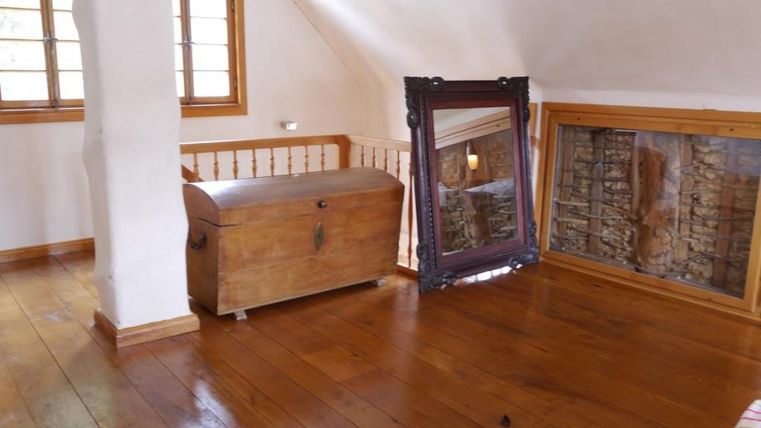 A bright room with wooden flooring and a large mirror. A wooden chest stands in the corner next to a window.