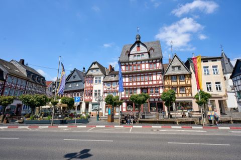 Ein malerisches Stadtbild mit Fachwerkhäusern und bunten Fahnen. Die Gebäude stehen an einer Straße unter einem klaren blauen Himmel.