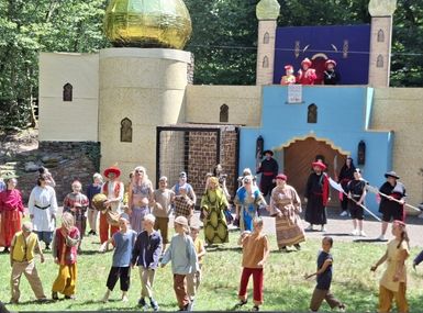  Freilichttheater mit großer orientalischer Bühnenkulisse, goldener Kuppel und zahlreichen kostümierten Darstellern sowie Kindern auf einer Waldbühne vor sommerlicher Naturkulisse.