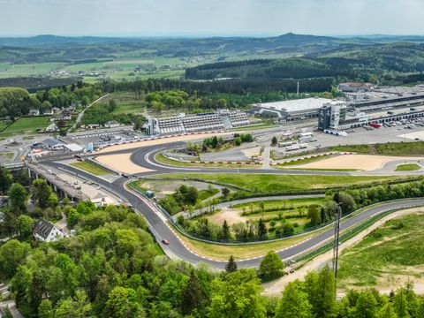 Eine Panoramaansicht einer Rennstrecke umgeben von grüner Landschaft. Im Hintergrund sind die Stände und andere Gebäude des Rennzentrums zu sehen.