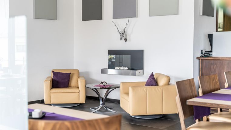 Ein modernes Wohnzimmer mit zwei bequemen Sesseln und einem Glastisch. An der Wand ist ein minimalistischer Kamin und eine dezente Dekoration.