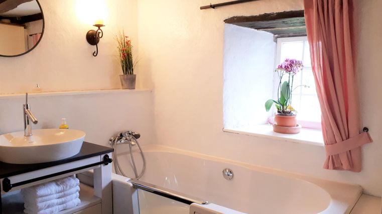 A cozy bathroom with a freestanding bathtub and a modern sink. A window with an orchid creates a pleasant atmosphere.
