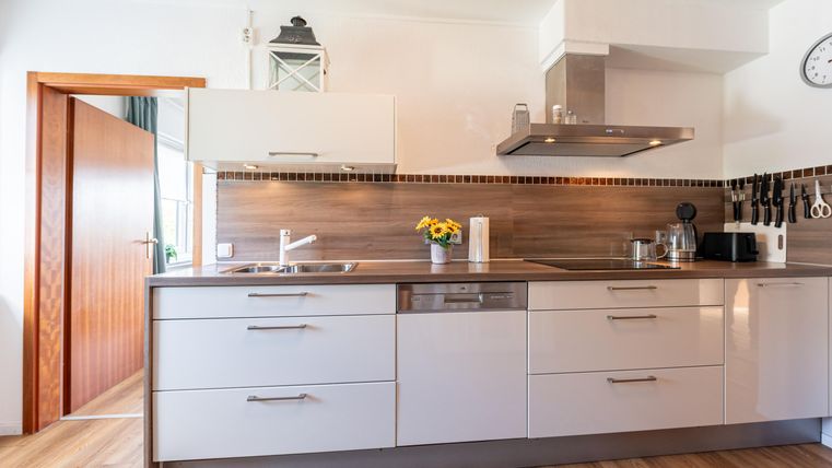 Een moderne keuken met lichte kasten en houten details. Op het aanrecht staan enkele keukentoestellen en een bloemenvaas.