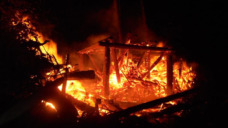 Een groot vuur brandt in de duisternis. Vlammen en verbrand hout zijn zichtbaar.