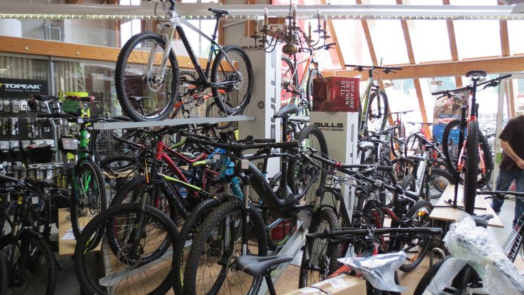 Ein Fahrradgeschäft mit vielen verschiedenen Fahrrädern und Zubehör. Die Räder sind ordentlich auf Regalen und im Raum verteilt.