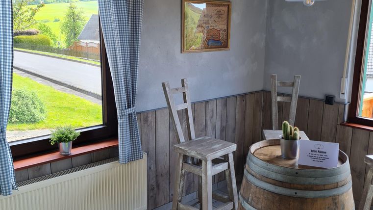 Een gezellige ruimte met een houten vat en twee stoelen. Door het raam valt veel daglicht naar binnen en je ziet het groene landschap buiten.