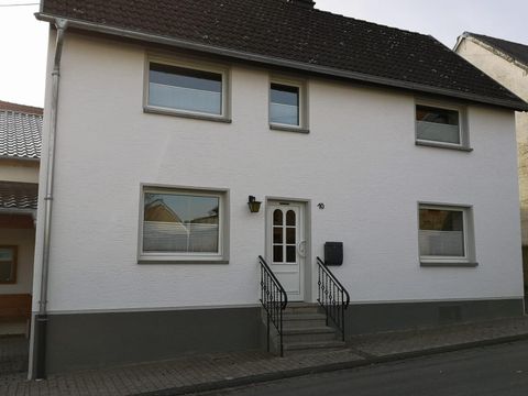 A modern two-story house with a white facade. In front of the entrance door, there is a small staircase and windows with shutters.