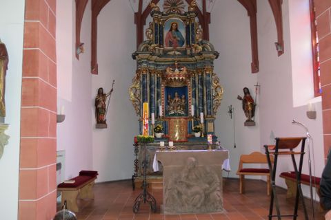 Een mooie kerkinterieur met een kunstzinnig vormgegeven altaar. De muren zijn versierd en er staan houten beelden naast het altaar.