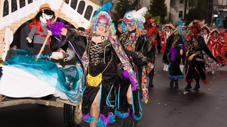 Een kleurrijke carnavalstoet met verklede mensen in levendige kostuums. De deelnemers dansen vrolijk en dragen kleurrijke accessoires.