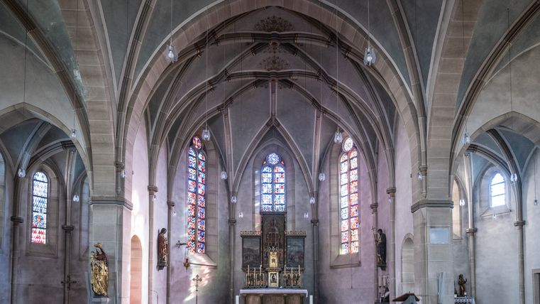 Innenansicht einer Kirche mit gotischen Bögen und bunten Glasfenstern.