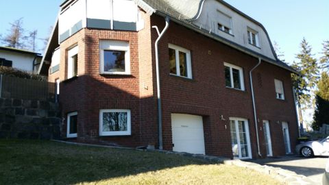 A modern two-story house made of red bricks. The garden is well-kept and the weather is sunny.