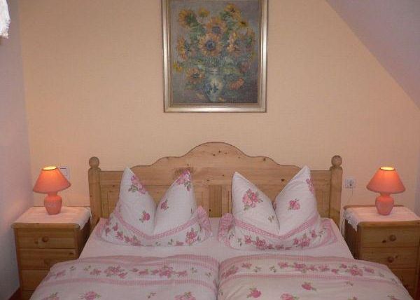 Une chambre confortable avec un lit en bois et du linge de lit à fleurs roses. À côté du lit se trouvent deux tables de nuit avec des lampes de table orange et un beau tableau au mur.