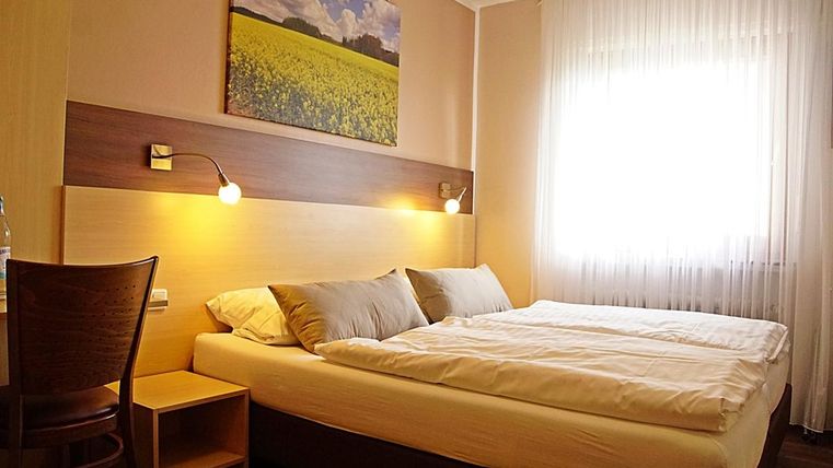 Une chambre d'hôtel confortable avec un lit double et une grande fenêtre.
Au mur, il y a une image d'un paysage fleuri.